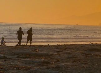 couple runs on beach with toddler keeping up on a bike